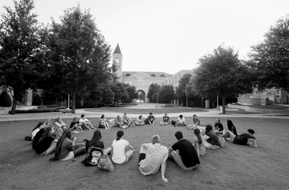 A group of students sitting in a circle on the campus lawn